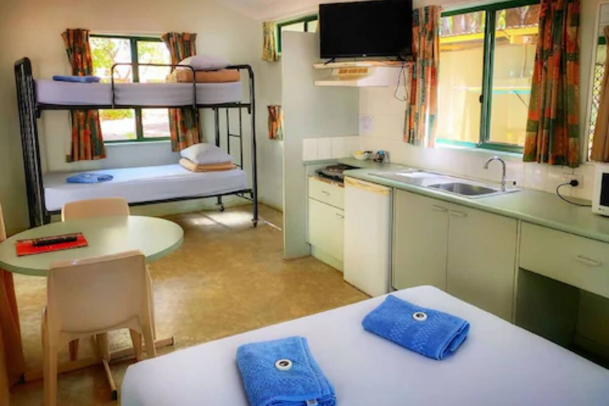 A compact hotel room with bunk beds, a small kitchenette, a television, and a dining area.