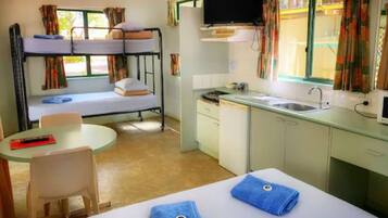 Een kleine hotelkamer met stapelbedden, een kitchenette, een televisie en een eethoek.