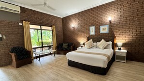 A spacious bedroom with a large bed, a sitting area with a table and chairs, and a view of greenery through a large window. - Knotts Crossing Resort (Katherine)