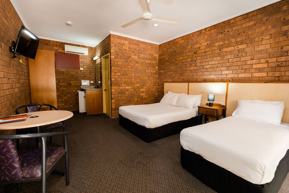 A hotel room with two beds, a desk, a chair, a TV, and a ceiling fan.