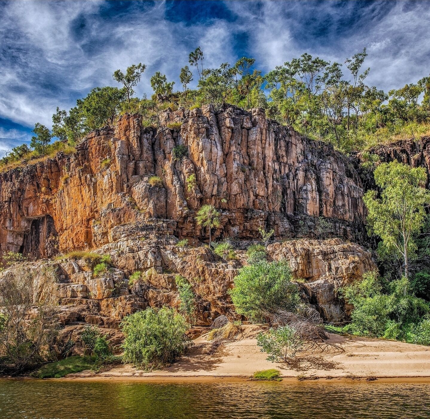 A rocky cliff with sparse vegetation and a river at the base.