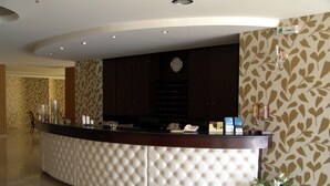 A reception desk with a tufted design, a clock, and a vase with flowers. - Hotel Merope (Samos)