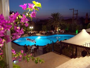 A swimming pool with a tiled deck, surrounded by outdoor seating and palm trees.