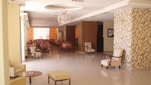 A spacious lobby with a chandelier, a dining area in the background, and a patterned wall. - Hotel Merope (Samos)