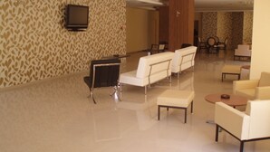A spacious lobby with a patterned wall, a flat-screen TV, and a seating area with sofas and a coffee table. - Hotel Merope (Samos)