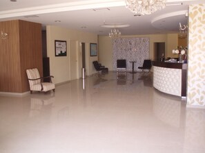 A spacious lobby with a reception desk, two armchairs, and a chandelier. - Hotel Merope (Samos)