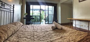 A bedroom with a large bed, a chair, and a table. There is a balcony with a view of the outside. - MC Mountain Home Apartelle (Alfonso)