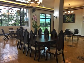 A dining area with a large table and chairs, a vase with flowers, and a view of greenery outside. - MC Mountain Home Apartelle (Alfonso)