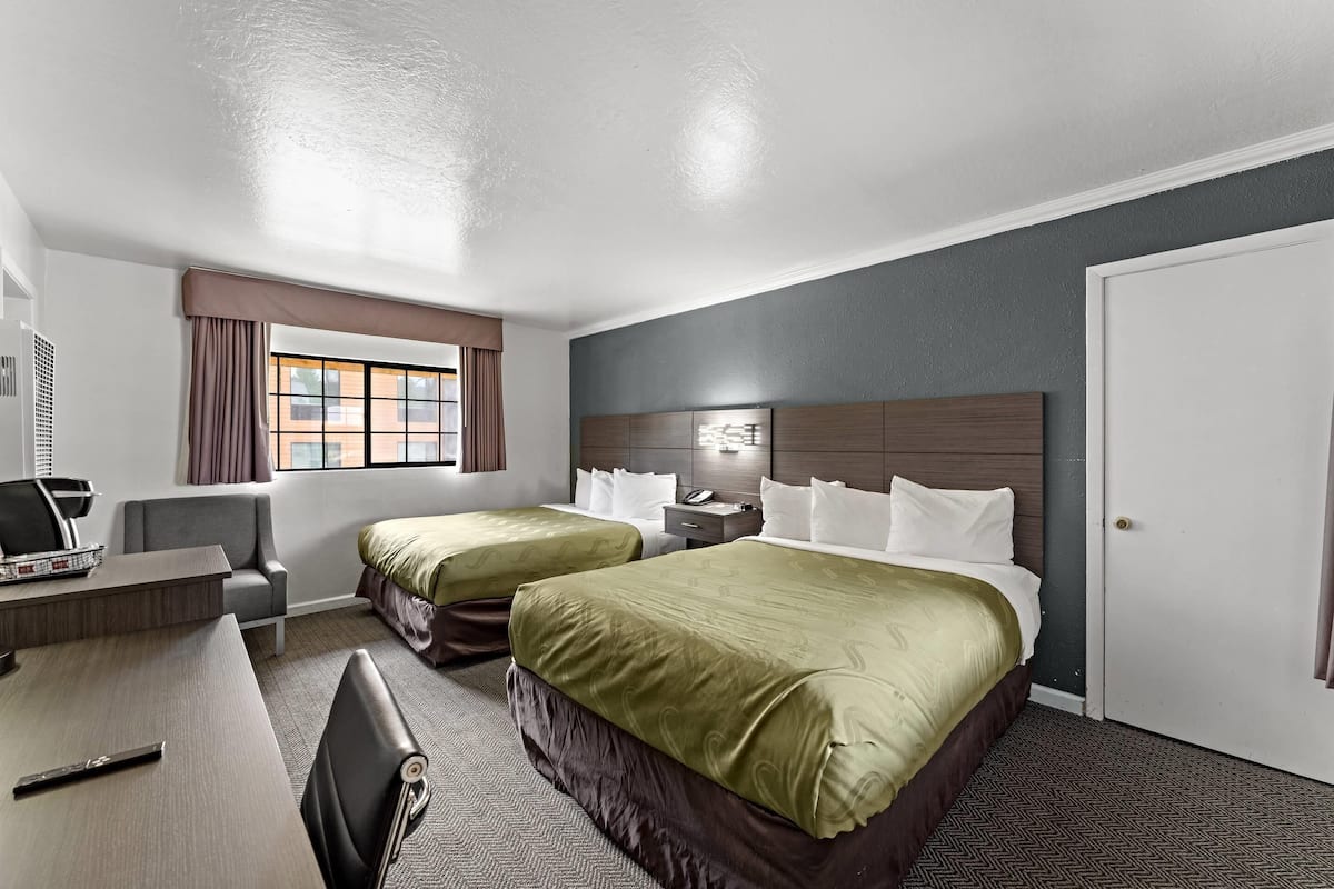 A hotel room with two beds, a desk, a chair, a window with curtains, a headboard, and a door.