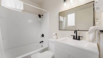 Un baño moderno con bañera, inodoro, lavabo y un espejo grande.
