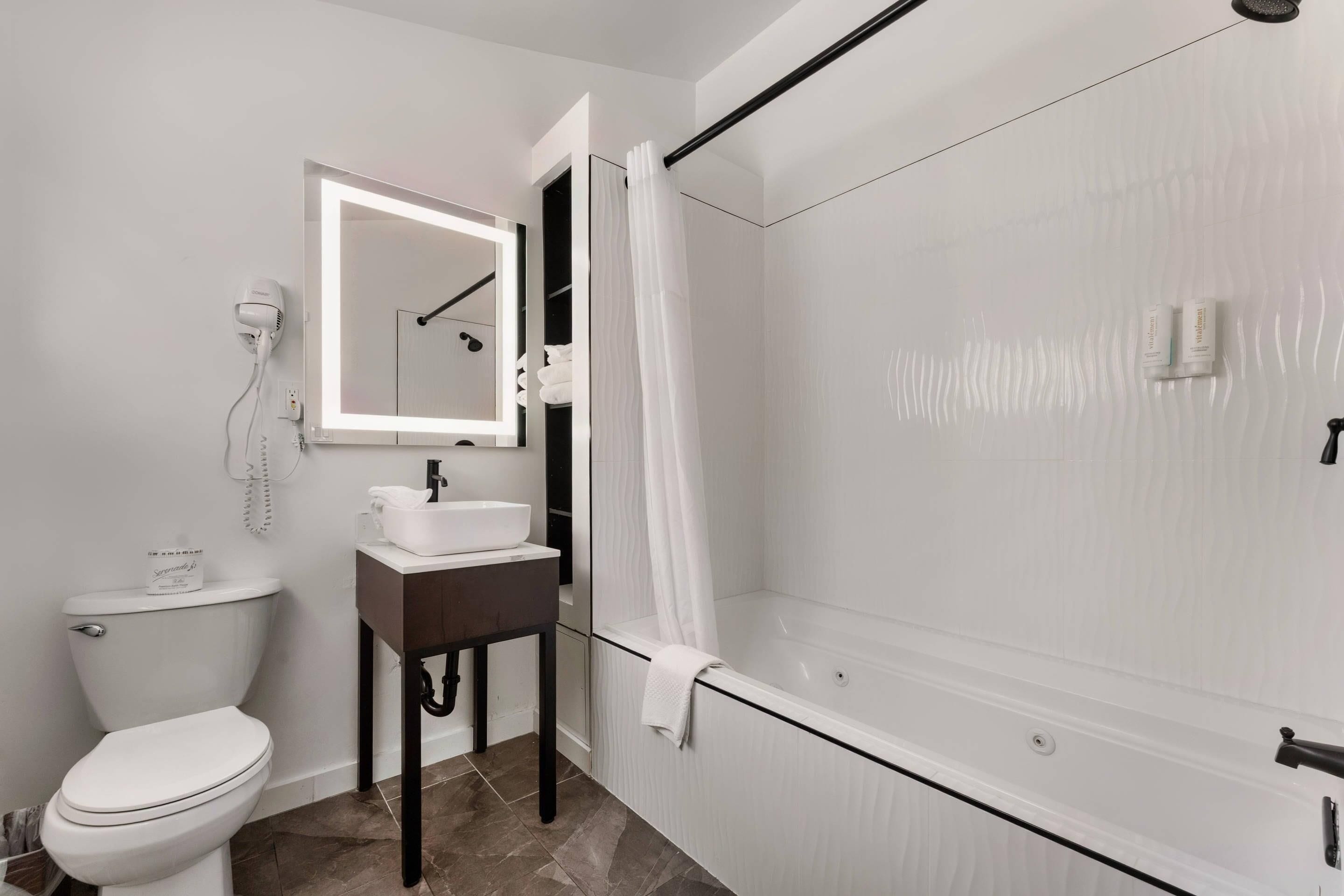 A bathroom with a toilet, sink, mirror, shower, and a towel rack.