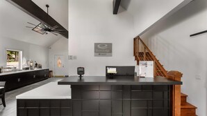Un comptoir d’accueil avec un plan de travail noir, un escalier en bois et une vue sur l’extérieur.