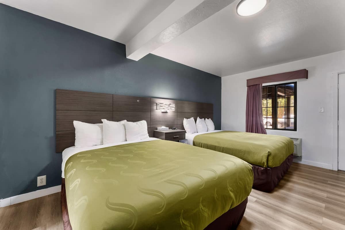 A hotel room with two beds, a nightstand, a window with curtains, and a ceiling light.