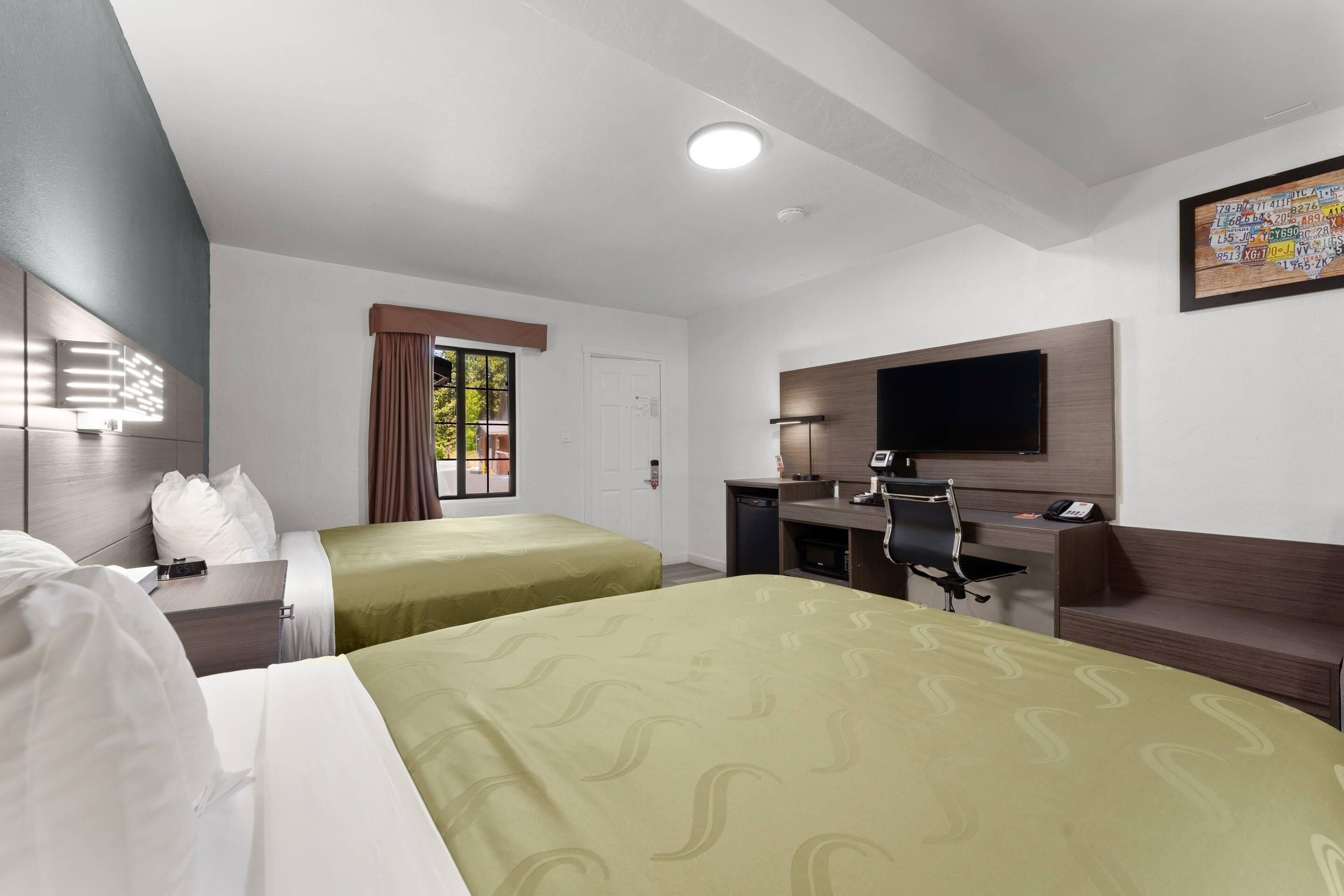 Une chambre d’hôtel avec deux lits, un bureau, une chaise, une télévision et une fenêtre avec des rideaux.