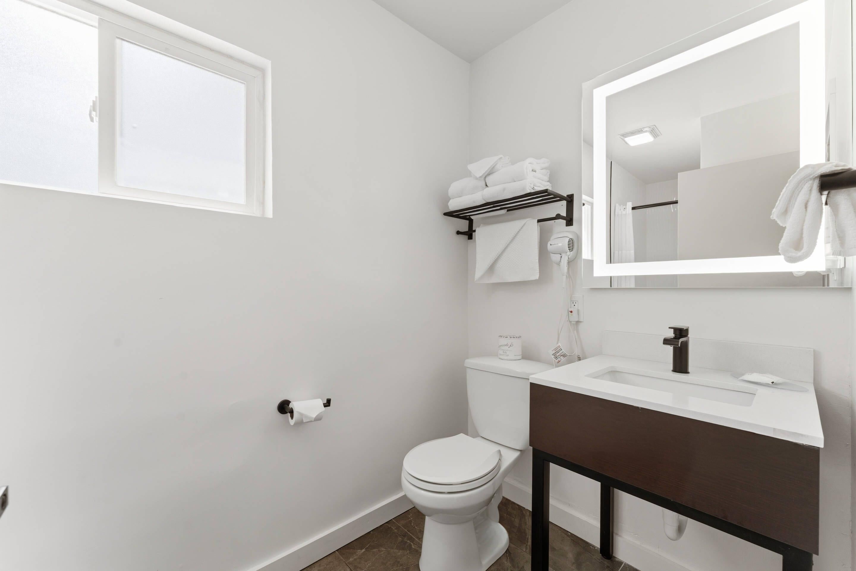 A bathroom with a toilet, sink, mirror, towel rack, and a window.