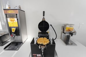 Un appareil à gaufres avec des gaufres en cours de préparation, un distributeur de sirop et un récipient rempli de sirop.