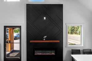 Un intérieur moderne avec une cheminée, une fenêtre donnant sur la rue et une porte menant à l’extérieur.