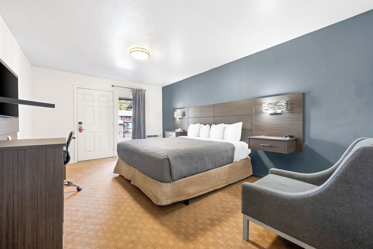 A bedroom with a bed, a desk, a chair, a nightstand, and a wall-mounted shelf.