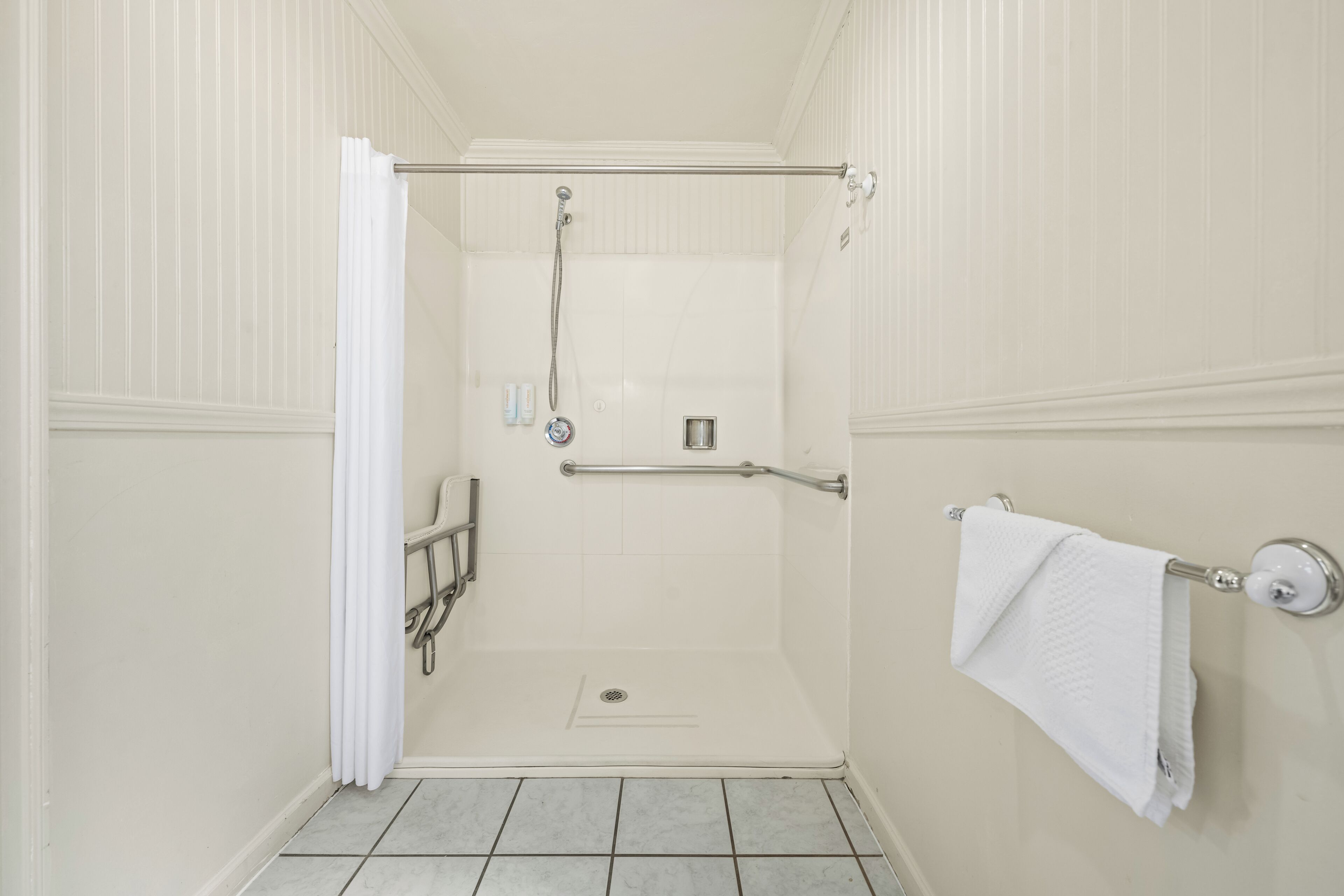 A walk-in shower with a grab bar, a white towel on a wall-mounted rack, and a white curtain partially open.