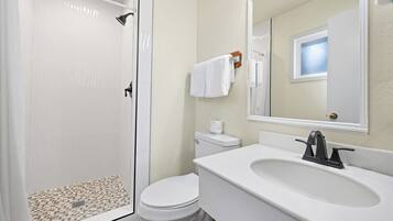 Un baño con ducha, inodoro, lavabo y espejo.