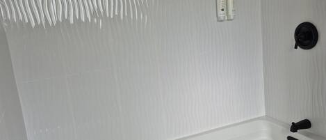 Een moderne badkamer met een groot bad, een handdouche en een wandmengkraan.