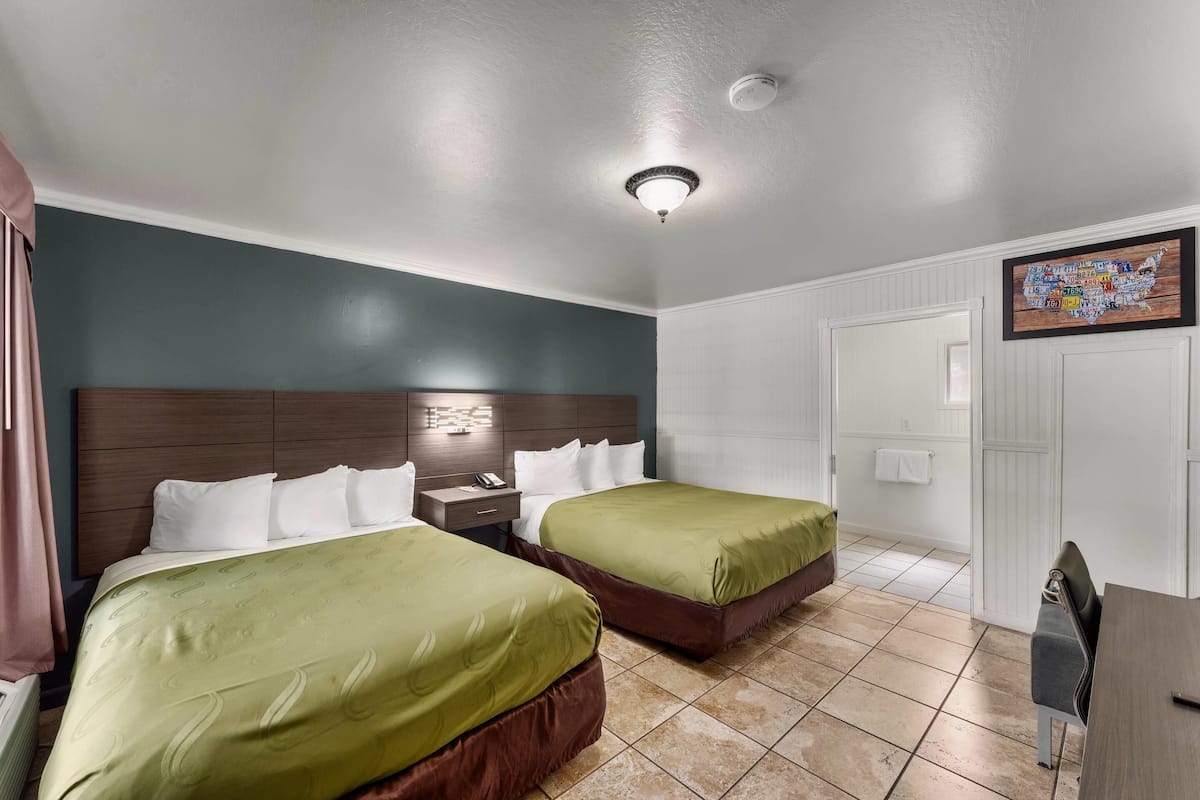 A hotel room with two beds, a nightstand, a desk, and a chair.