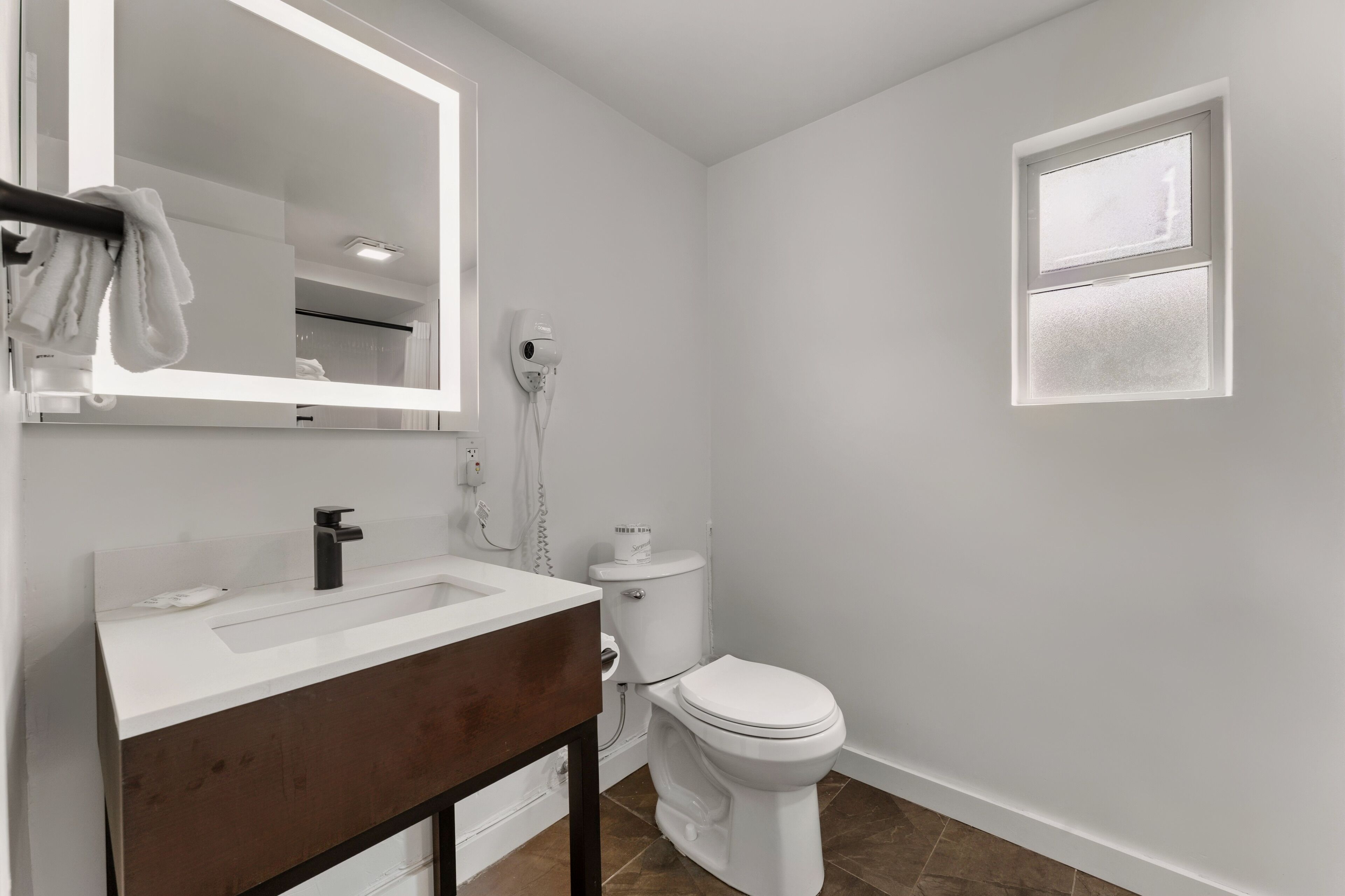 Un baño con lavabo blanco, un espejo, un inodoro y una ventana.