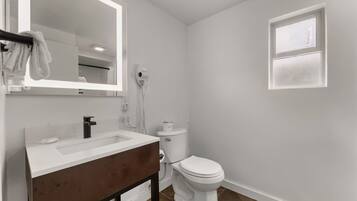 Un baño con lavabo blanco, un espejo, un inodoro y una ventana.