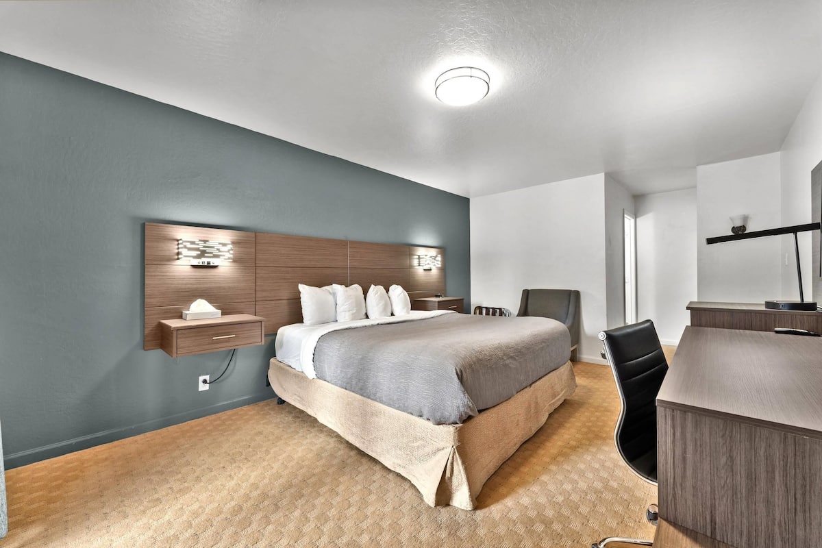 A hotel room with a bed, bedside table, desk, chair, and a large mirror.