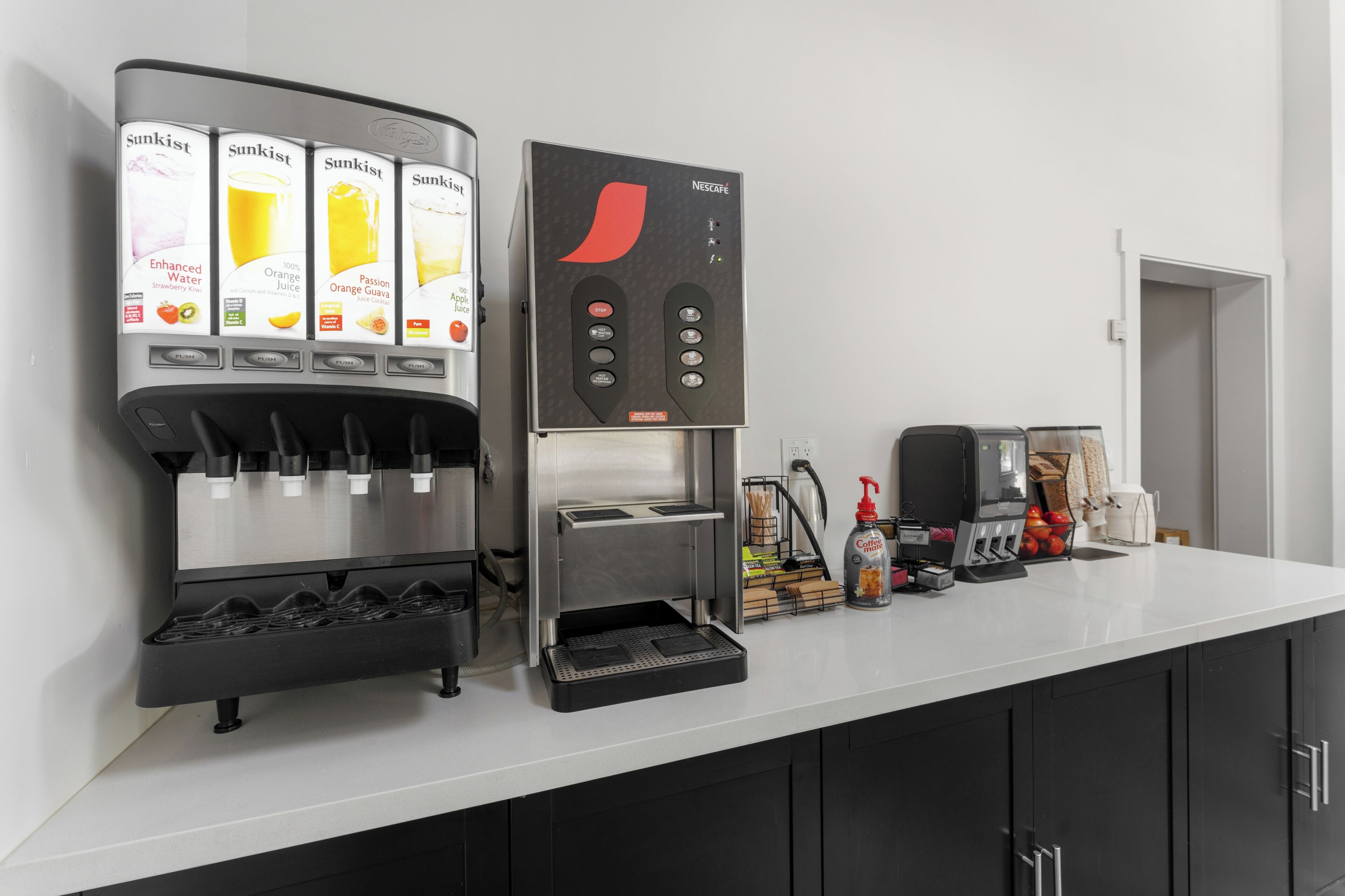 Een moderne keuken met een koffieapparaat, een sapdispenser en een koffiemachine.