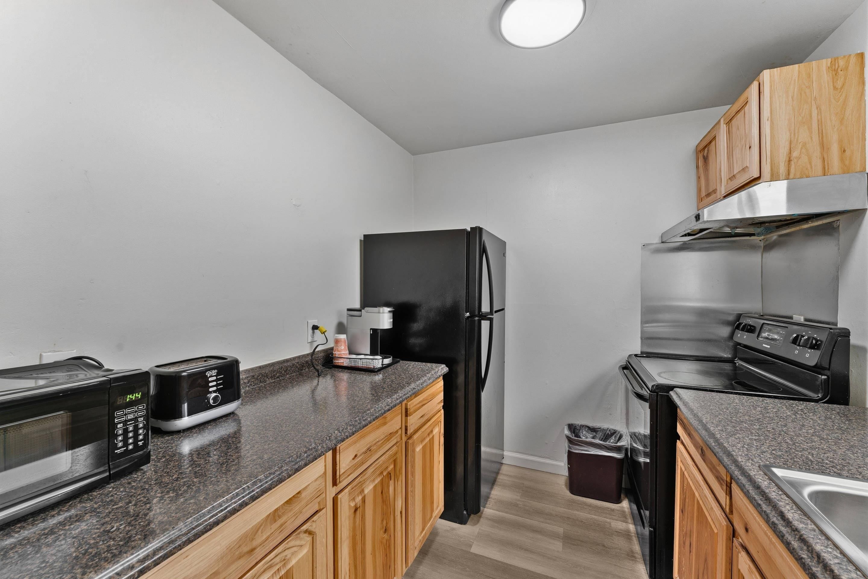 A compact kitchen with a microwave, toaster, refrigerator, oven, and wooden cabinets.