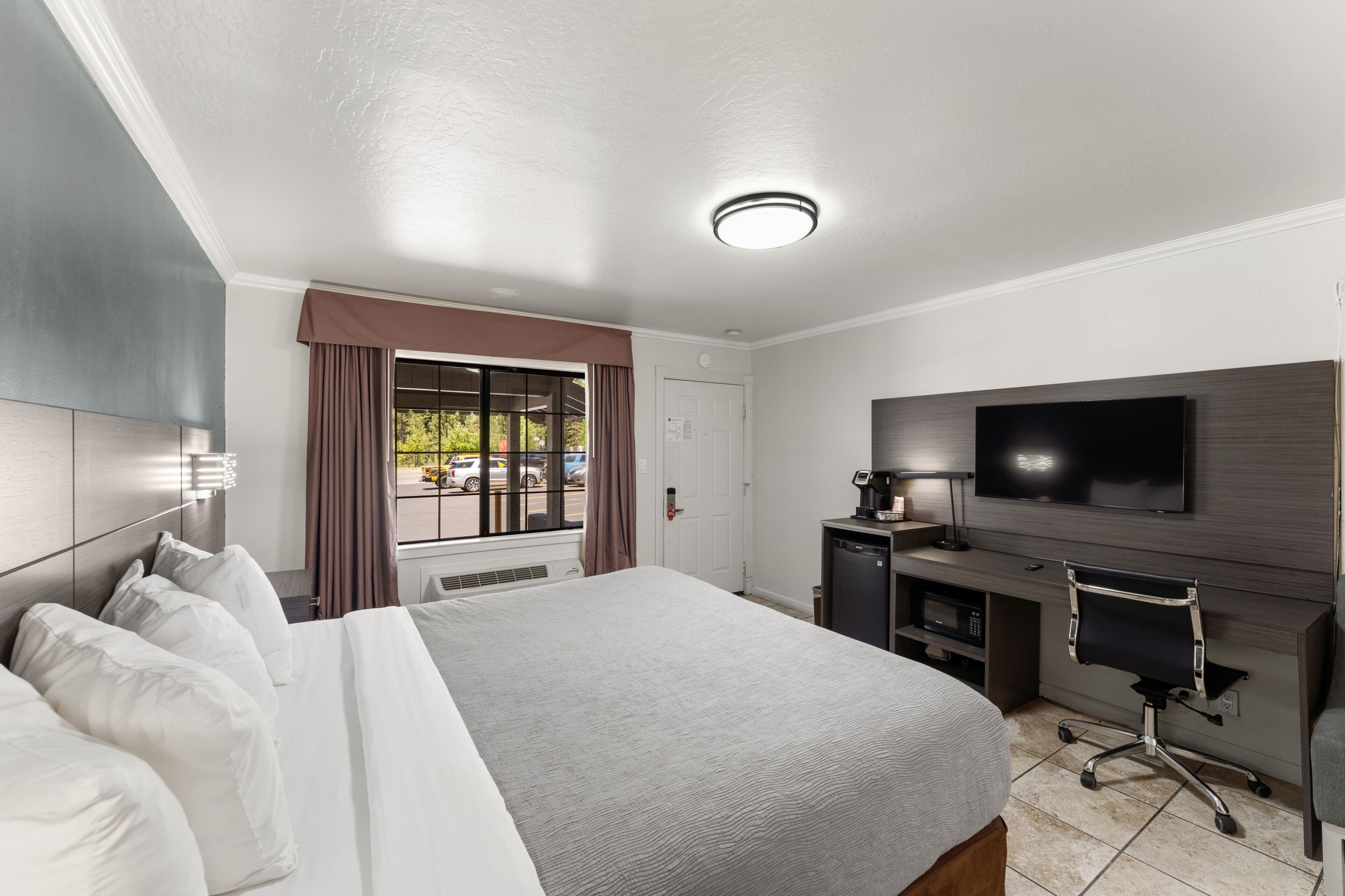 Una habitación de hotel con cama, escritorio, silla, televisión y ventana con cortinas.