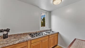 A kitchen with a gas stove, sink, wooden cabinets, a window with a view, and a countertop with utensils.