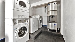 Une buanderie équipée de machines à laver et de sèche-linge superposés, d’un distributeur d’eau et d’une petite marche menant aux appareils.