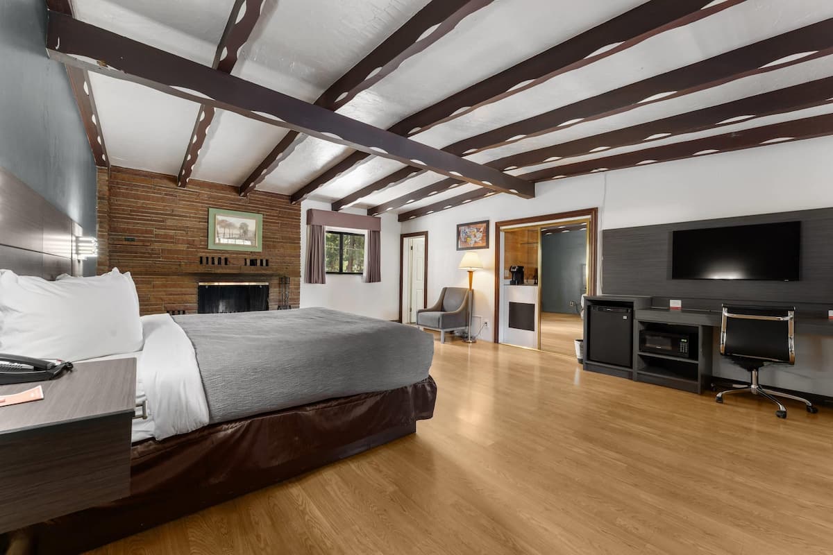 A modern hotel room with a large bed, a desk, a TV, and a fireplace.