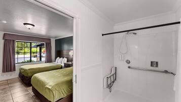 A hotel room with two beds, a shower with grab bars, a window with curtains, and a view of the outdoors.