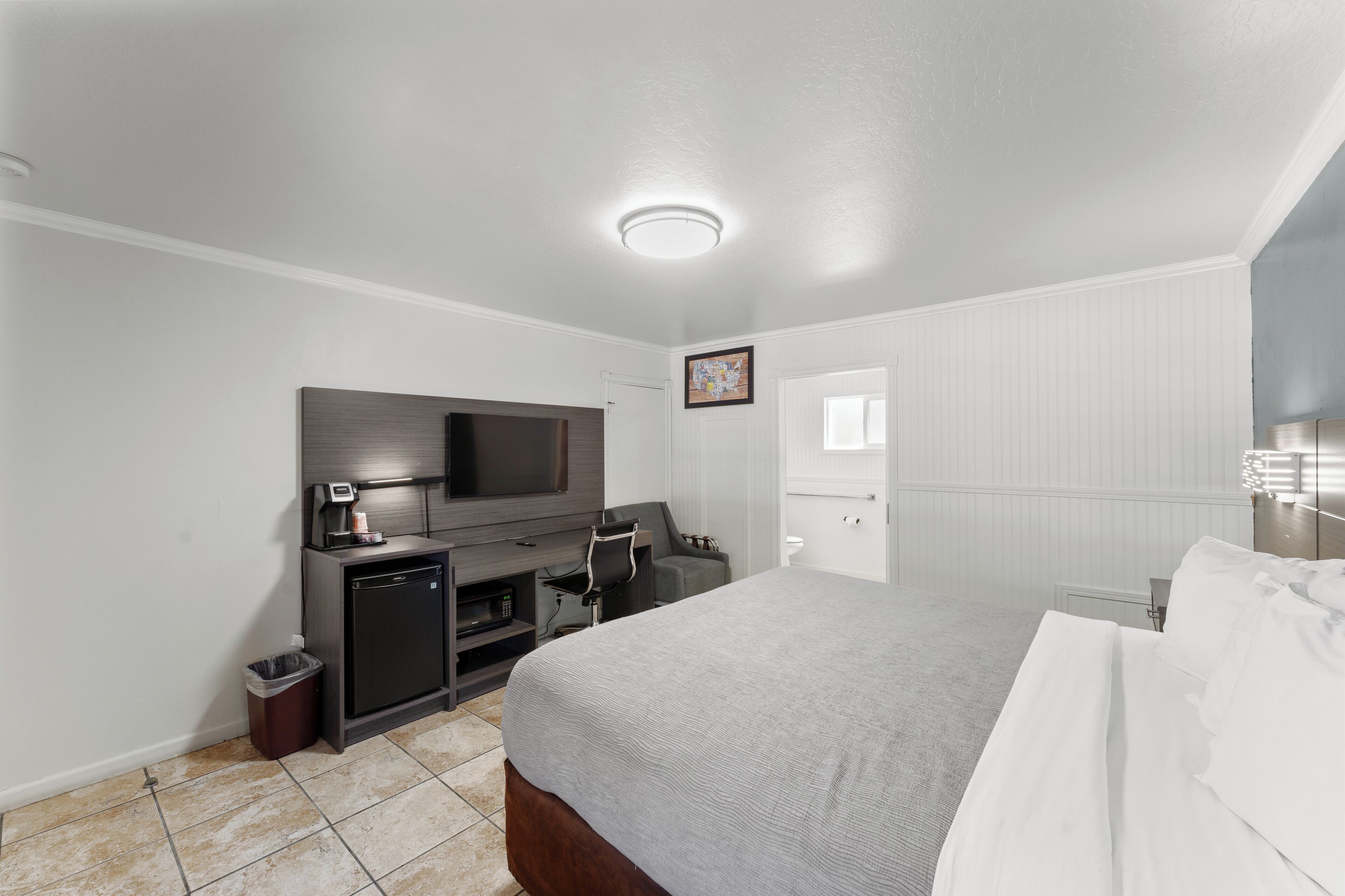 A hotel room with a bed, a desk with a computer, a TV, and a small kitchenette.