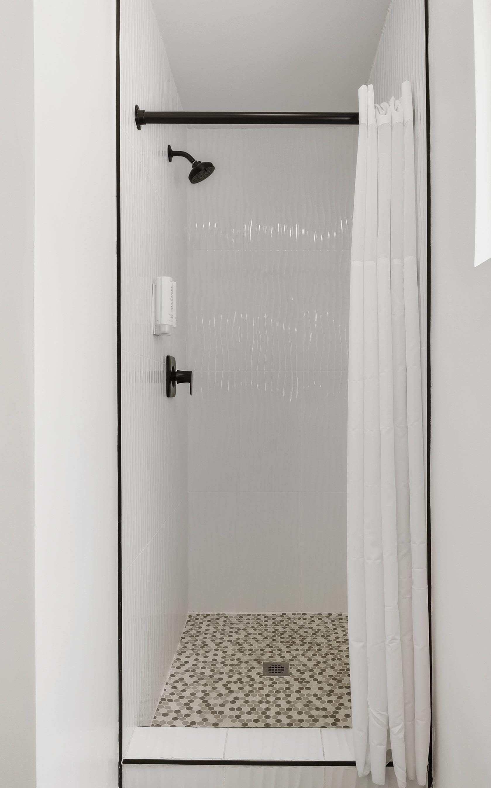 Een douche met een glazen deur, een douchekop en een betegelde vloer.