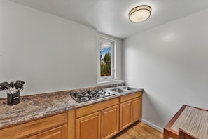 A kitchen with a gas stove, sink, wooden cabinets, a window with a view, and a countertop with utensils. - Econo Lodge Inn & Suites Heavenly Village Area (South Lake Tahoe)