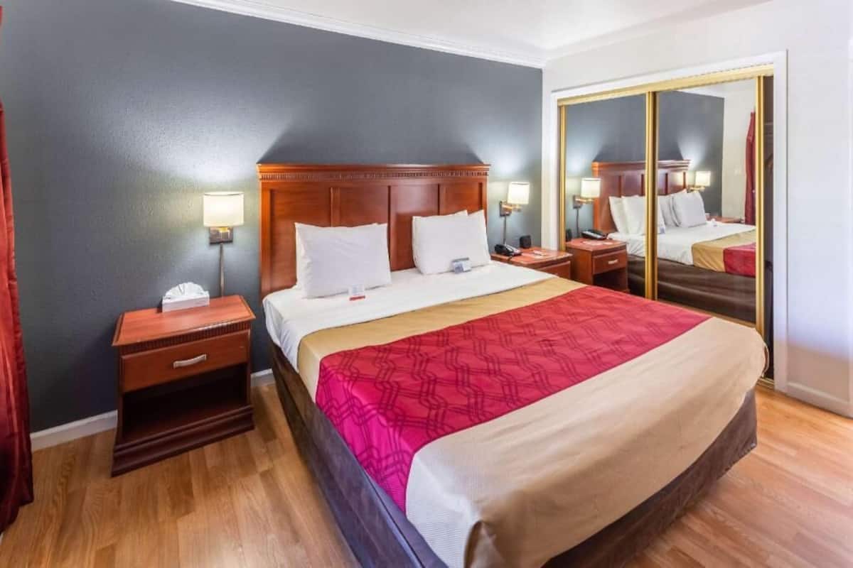 A hotel room with a large bed, a nightstand, a mirror, and a wardrobe.
