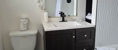 Une salle de bain avec des toilettes blanches, un meuble-lavabo en bois foncé, un miroir et un porte-serviettes.