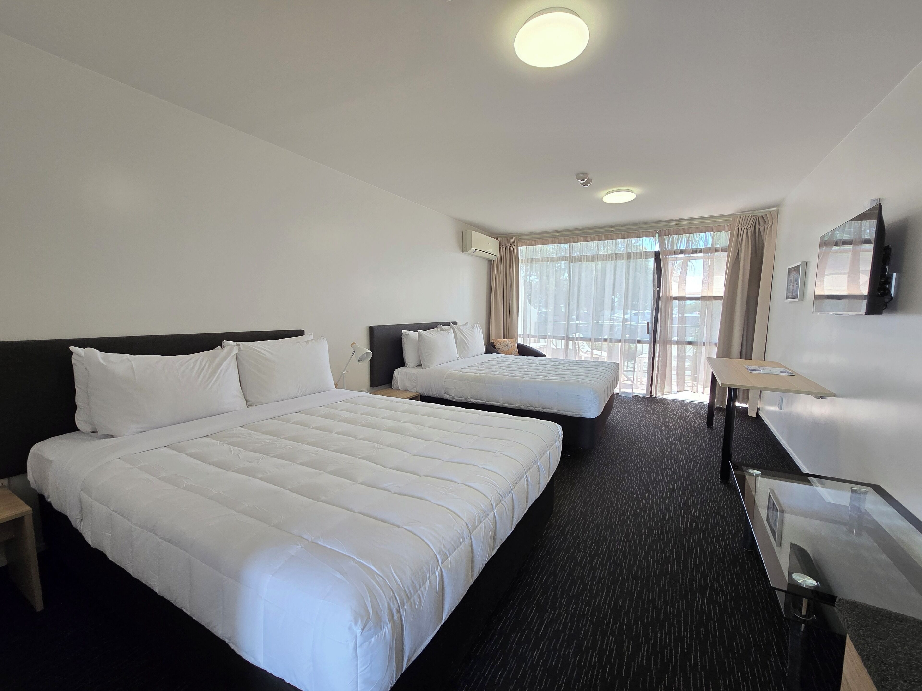 A hotel room with two beds, a desk, and a TV.