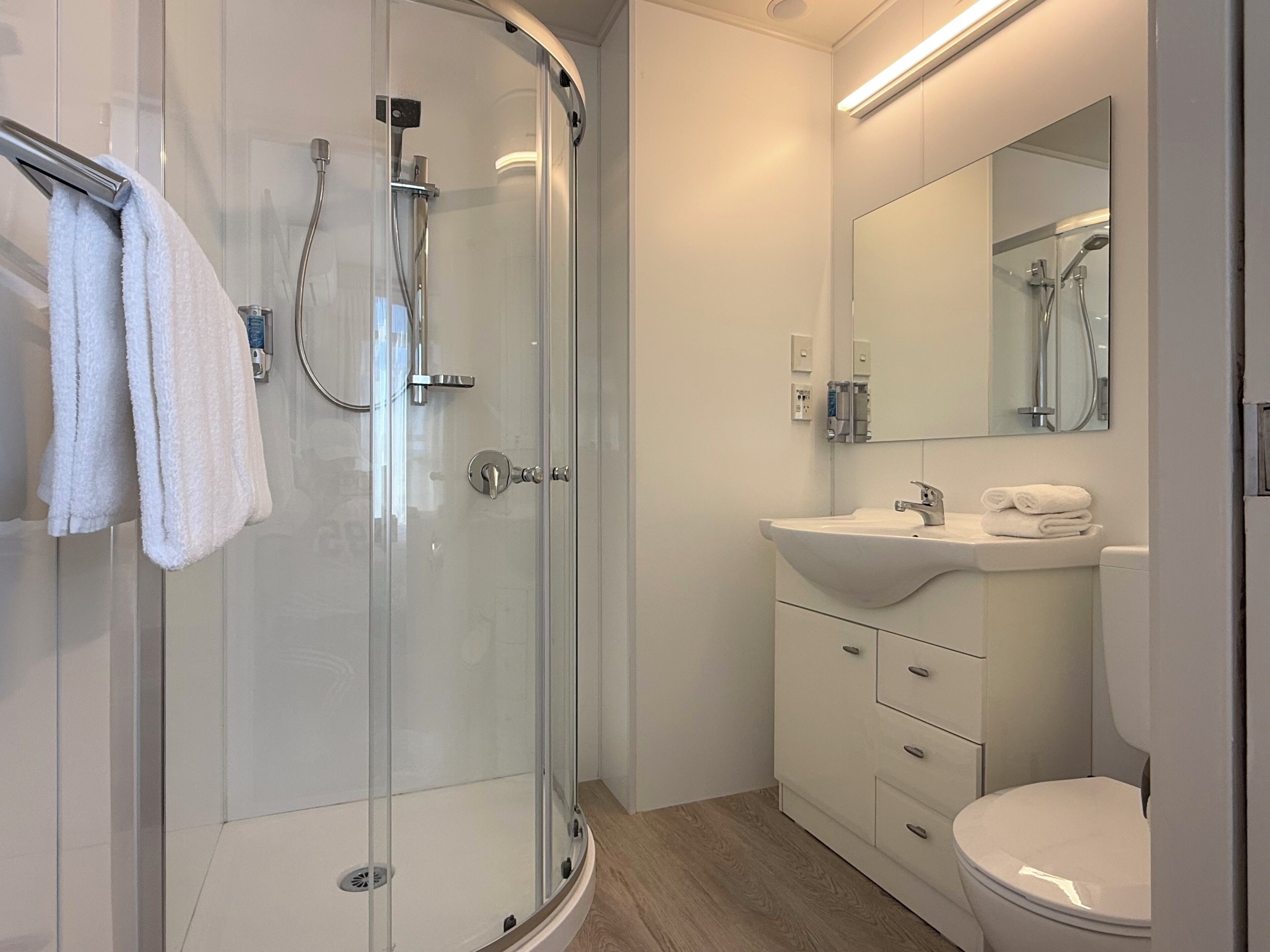 Un baño moderno con ducha de vidrio, lavamanos blanco y espejo sobre el tocador.