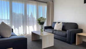 Un salon moderne avec un canapé en cuir noir, une table basse en bois et un vase rempli de fleurs.