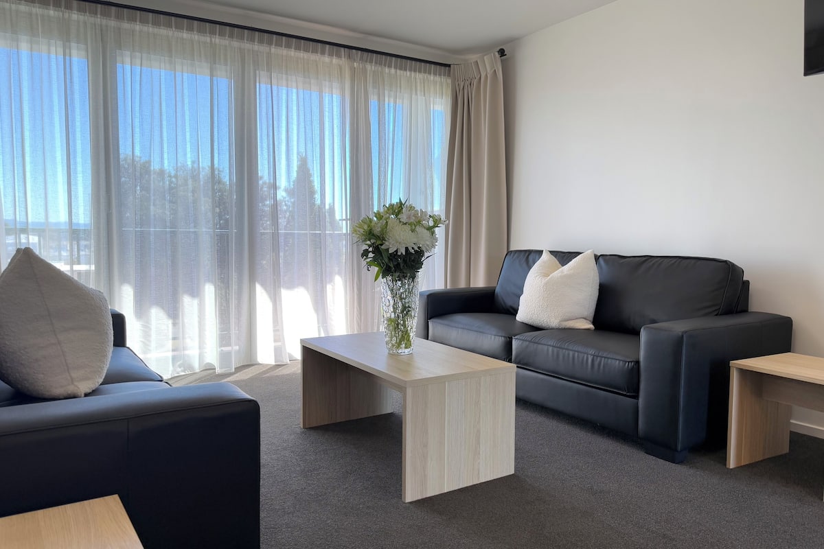 Un salón moderno con un sofá de cuero negro, una mesa de centro de madera y un jarrón con flores.