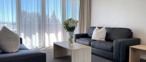 A modern living room with a black leather sofa, a wooden coffee table, and a vase with flowers.
