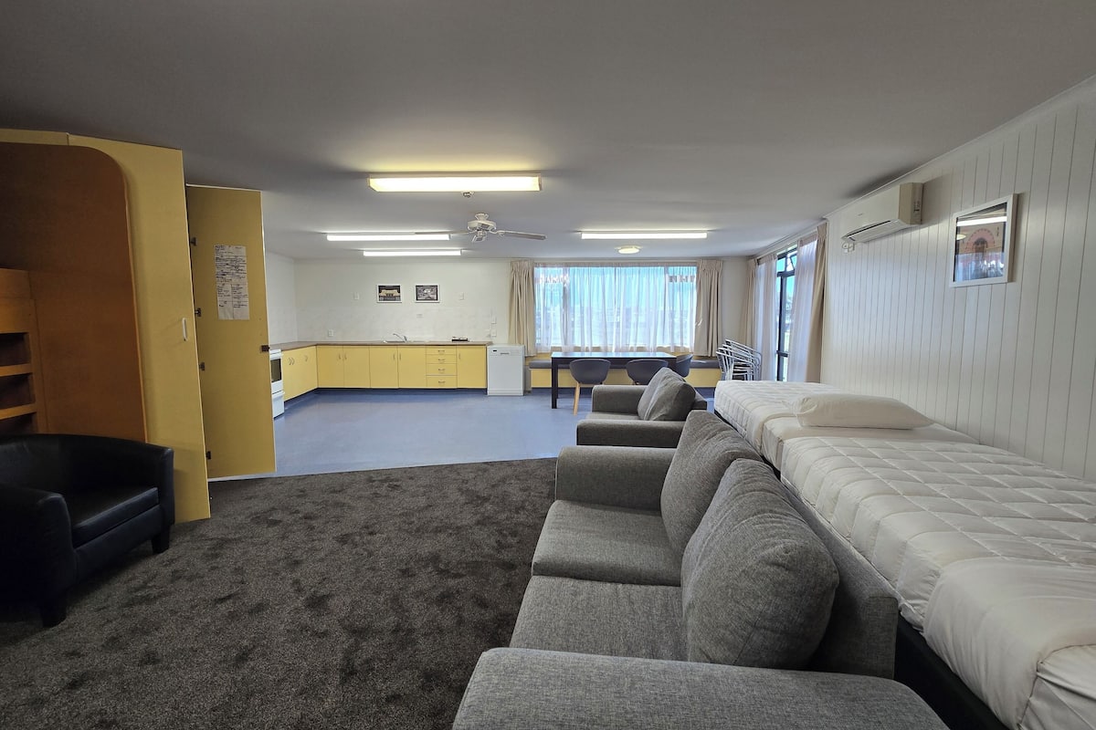 Una habitación de hotel compacta con kitchenette, sofá, cama y zona de comedor con mesa y sillas.