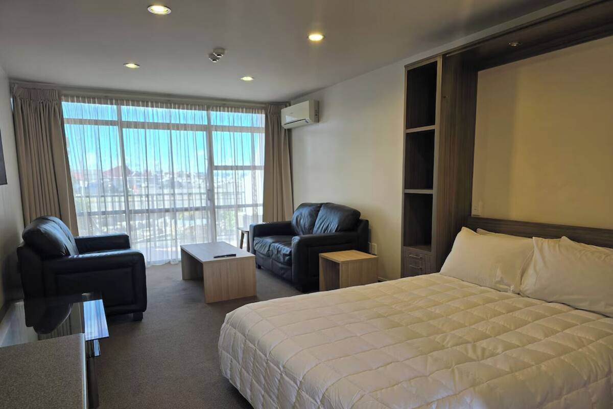 Habitación de hotel con una cama grande, dos sofás, una mesita y un ventanal con cortinas.