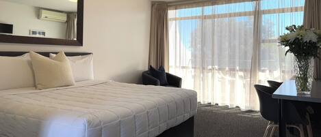 Una habitación de hotel con una cama grande, una silla, una mesa y un florero con flores.