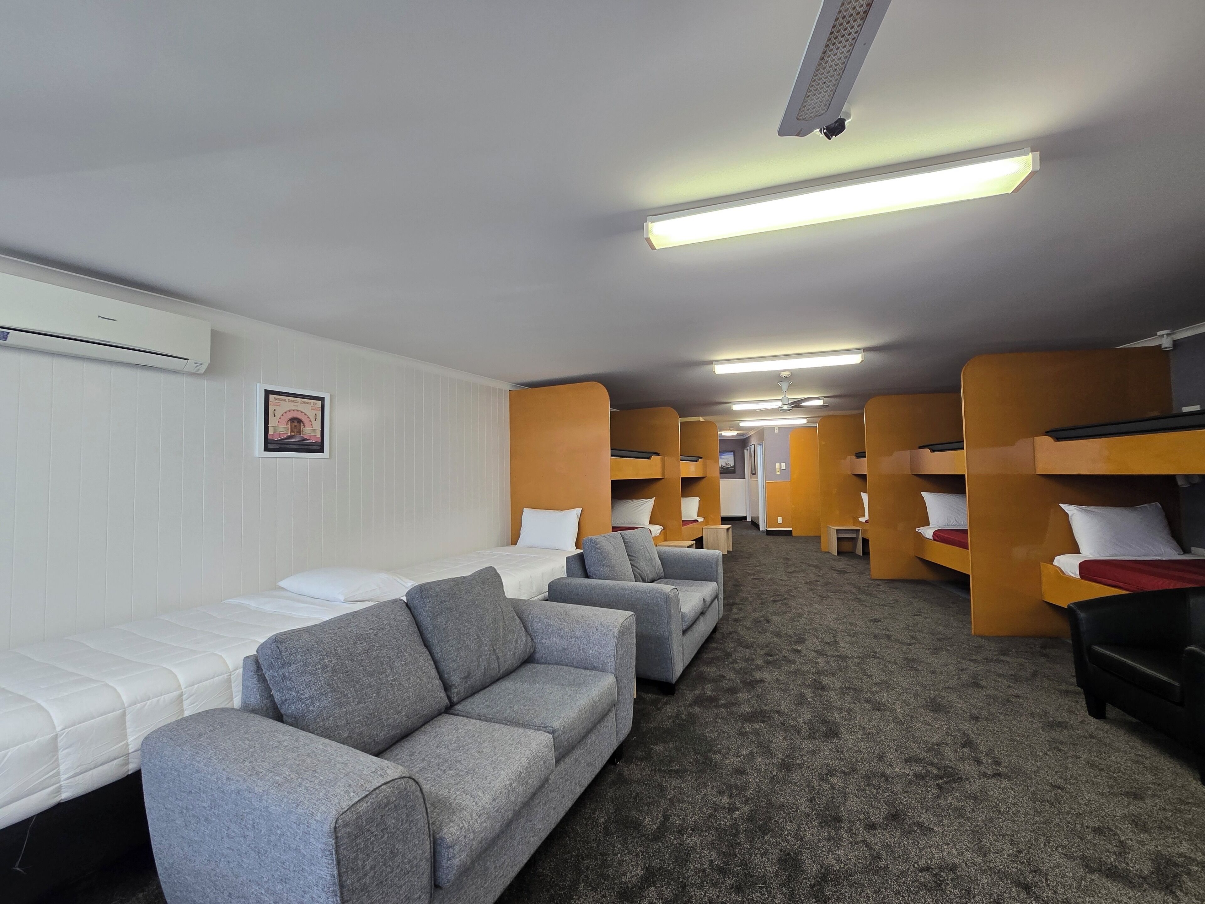 Una habitación con literas, un sofá y una cama. Hay un ventilador de techo y un equipo de aire acondicionado.